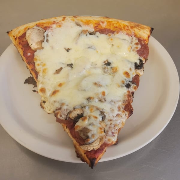 A Free Wheeler Pizza slice with melted cheese, pepperoni, and mushrooms on a white plate.