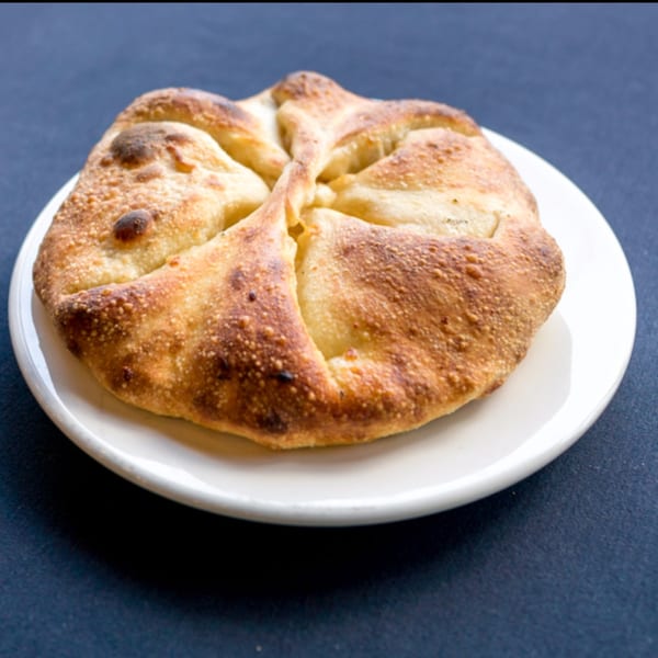 Golden-brown Free Wheeler Pizza calzone, with a crimped top, on a white plate against a dark background.