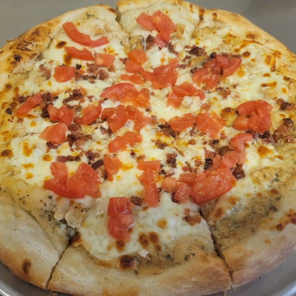 A Free Wheeler Pizza with white sauce, melted cheese, diced tomatoes, and bacon bits.