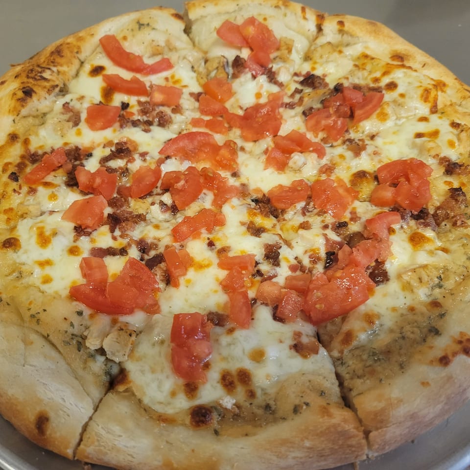 A Free Wheeler Pizza with white sauce, melted cheese, diced tomatoes, and bacon bits.