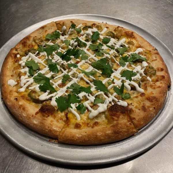 A Free Wheeler Pizza with green chiles, cilantro, and a white sauce drizzle on a metal tray.