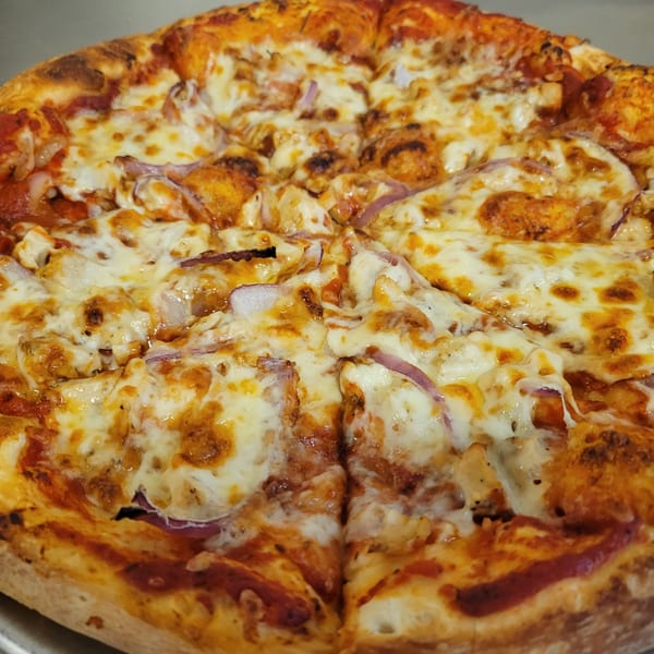 Close-up of a Free Wheeler Pizza with melted cheese, chicken, and red onions.