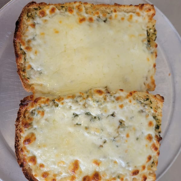 Two slices of cheesy garlic bread, golden brown and bubbling, on a metal tray.