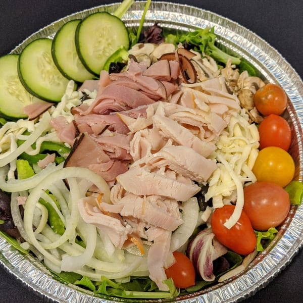 A large salad in a foil pan with ham, turkey, cheese, cucumbers, onions, and tomatoes.